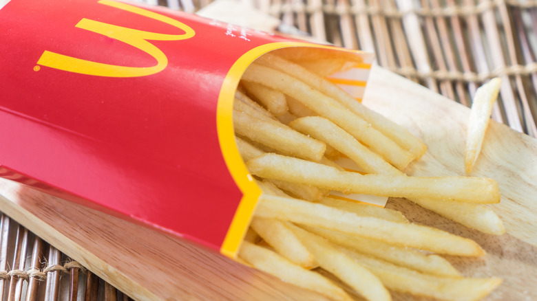 The iconic red fry box from McDonald's laying on its side with fries spilling out onto a board.