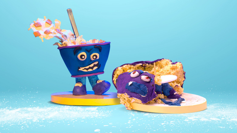 A cake shaped like an anthropomorphic blue and purple cereal bowl with a face and two feet next to a mangled, horribly made version of the same cake on