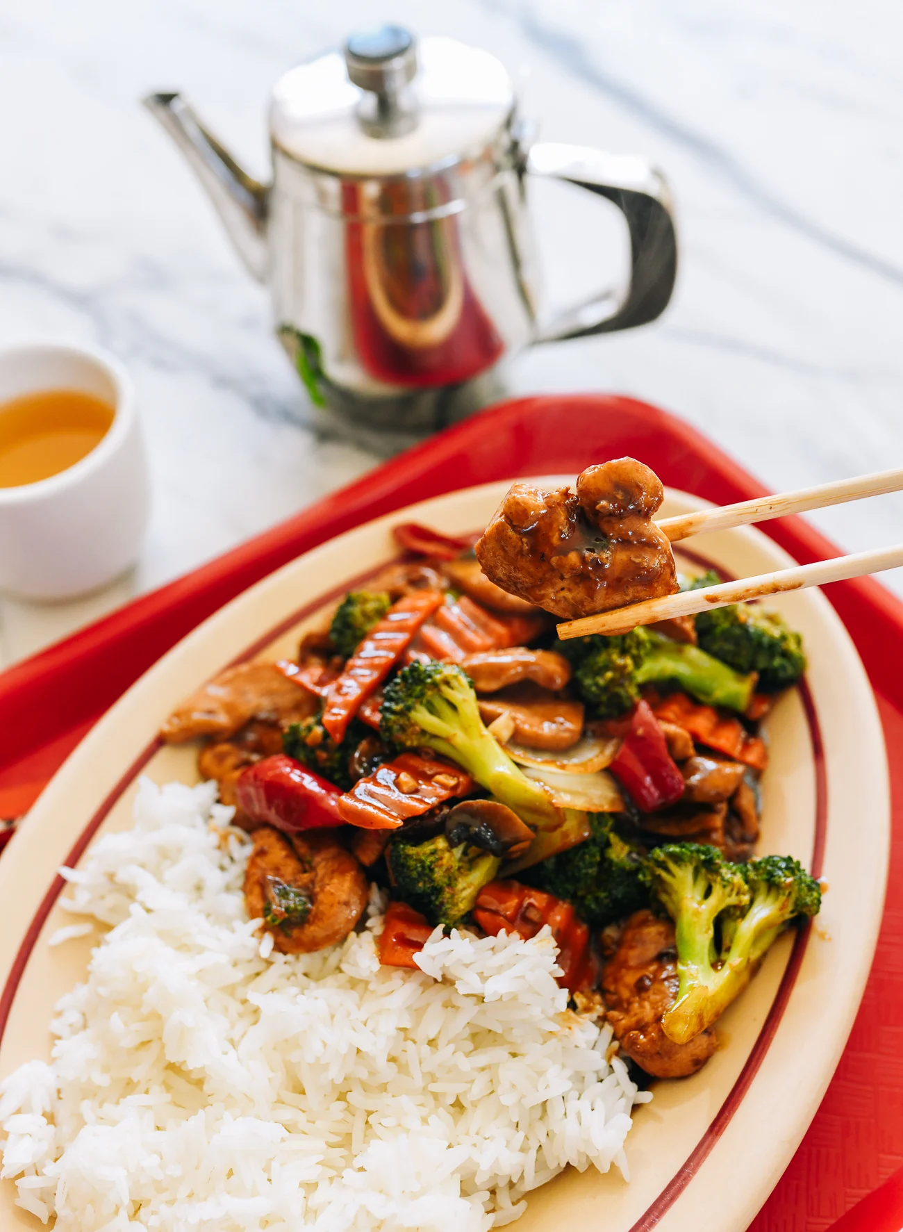 Picking up piece of Chinese takeout chicken with mixed vegetables with chopsticks
