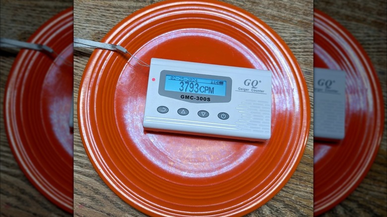 Vintage red Fiestaware plate with a Geiger counter placed on top, reading 3793 CPM.
