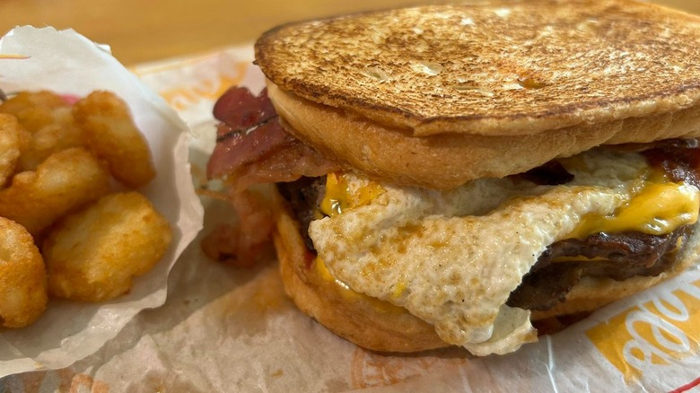 A Hardee's Frisco Breakfast Burger with tater tots