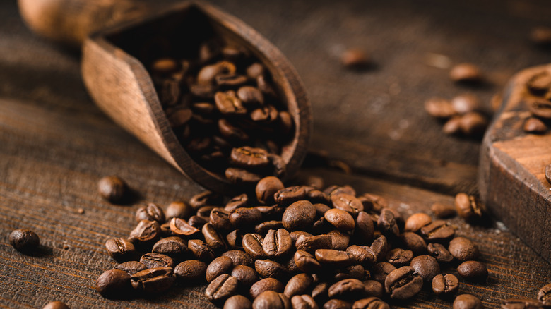 Whole coffee beans on a wooden table with a wooden scoop