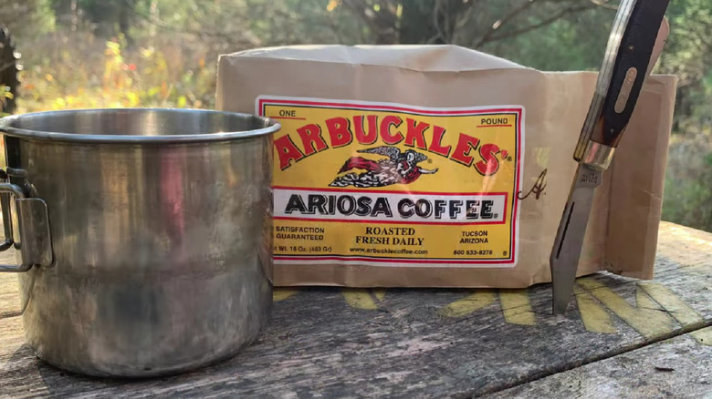 Bag of Arbuckles' coffee on a wood table along with a pot and a pocket knife