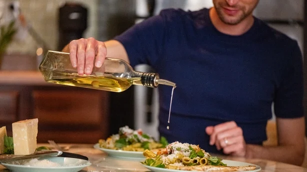 man pouring olive oil onto his dinner