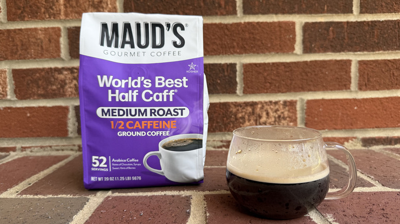 Bag of half-caff ground coffee with image of coffee mug, standing in front of brick wall