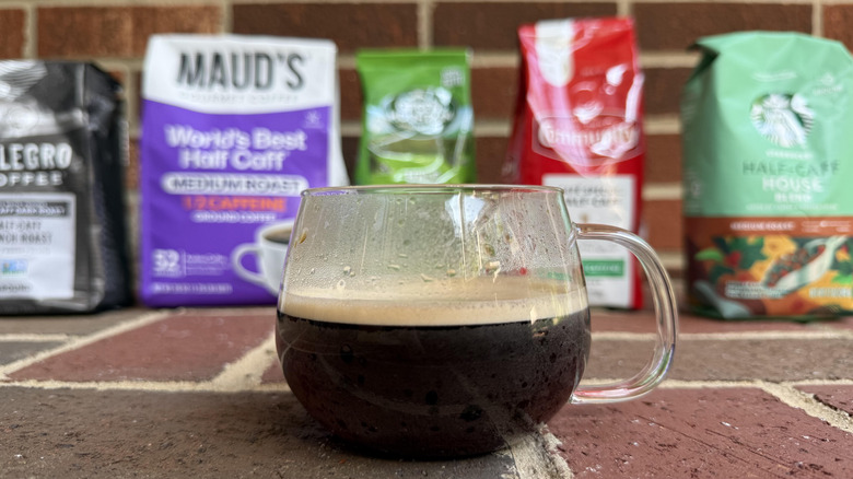 Glass mug of coffee placed in front of several bags on brick surface