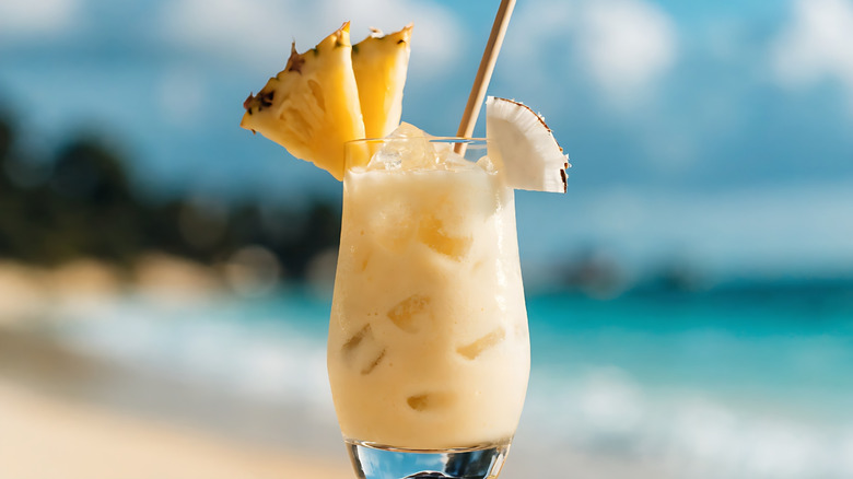 Piña colada garnished with fruit in front of a blurred beach background