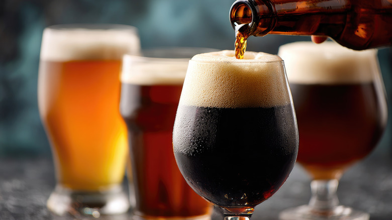 Assortment of different types of beer in a variety of glasses with dark beer being poured in front