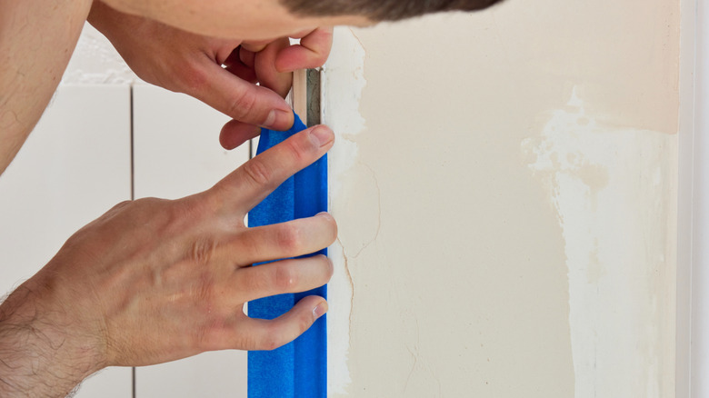 A person pressing painter's tape between a wall and tiles