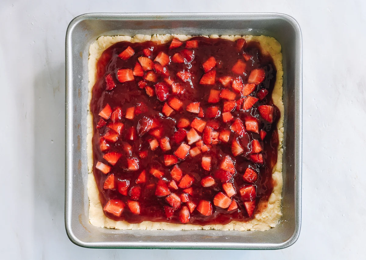 diced strawberries scattered on top of dough with strawberry jam