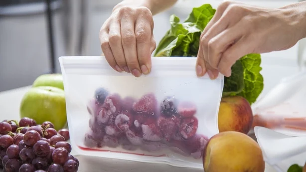 A young mother puts frozen raspberries into a clear food storage bag. 