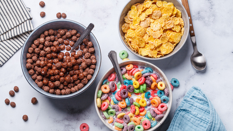 Three bowls filled with chocolate puffs, fruit loops, and corn flakes.