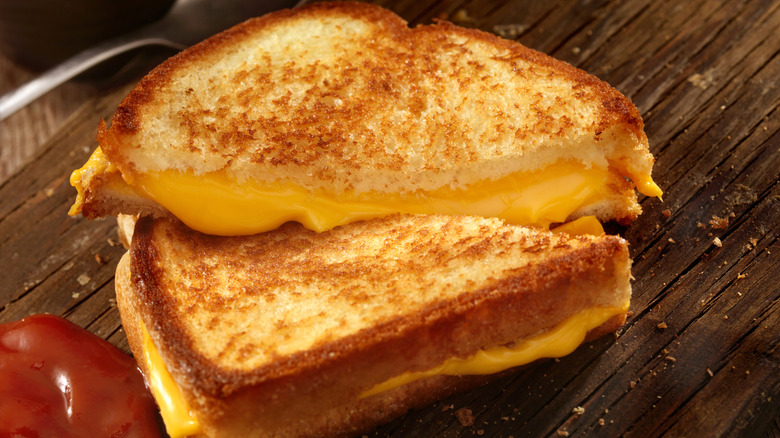 Two slices of grilled cheese with cheese oozing out on a table beside a squirt of ketchup.