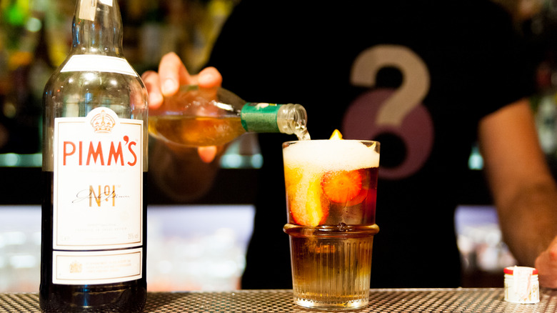 Barman making a quick British classic Pimm's cocktail indoor on bar top with branded bottle