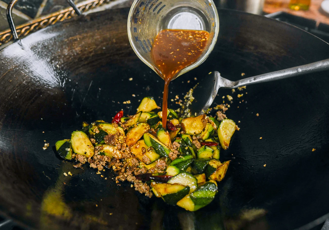 pouring sauce mixture into wok with zucchini and ground pork