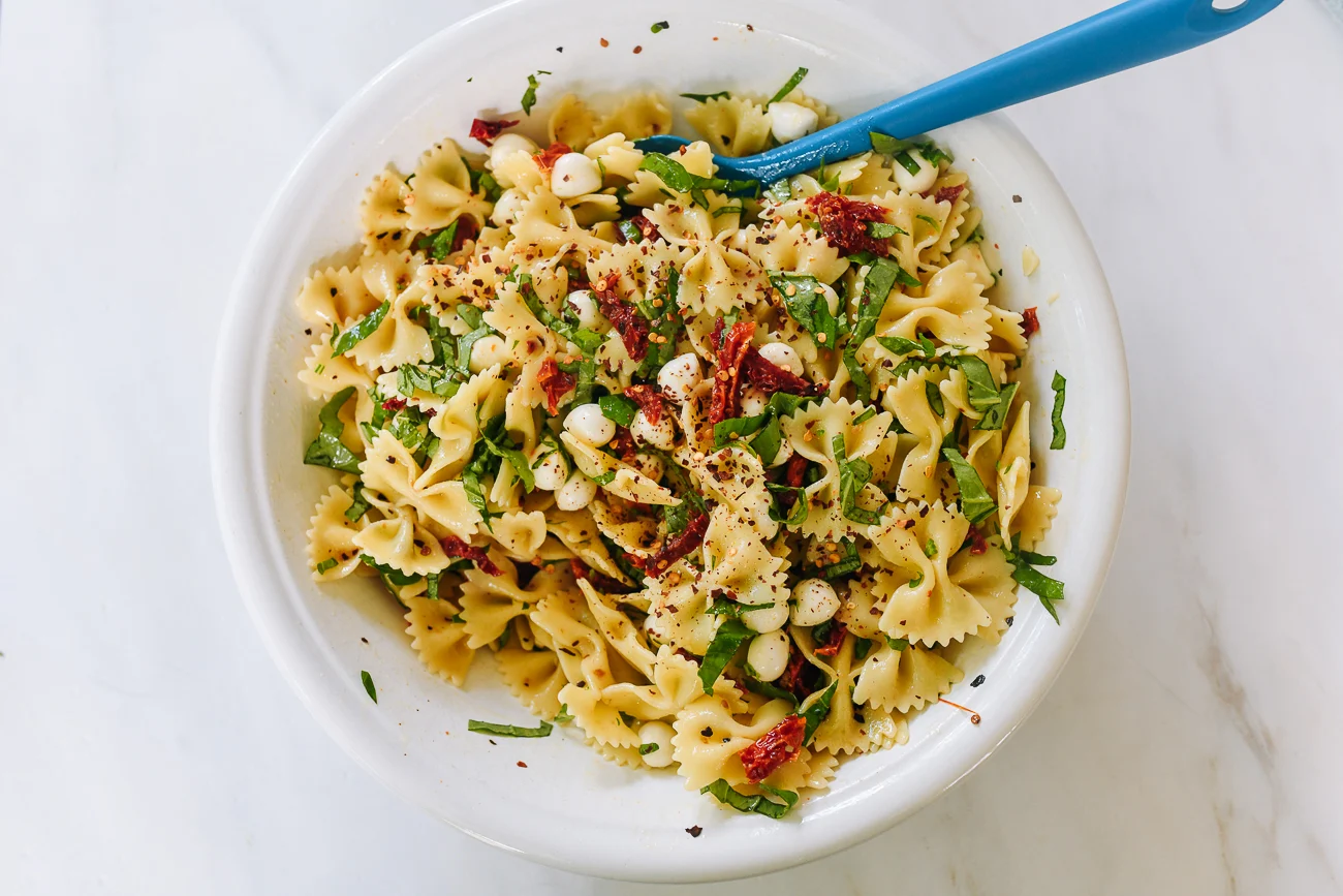 mixing spicy sun-dried tomato pasta salad