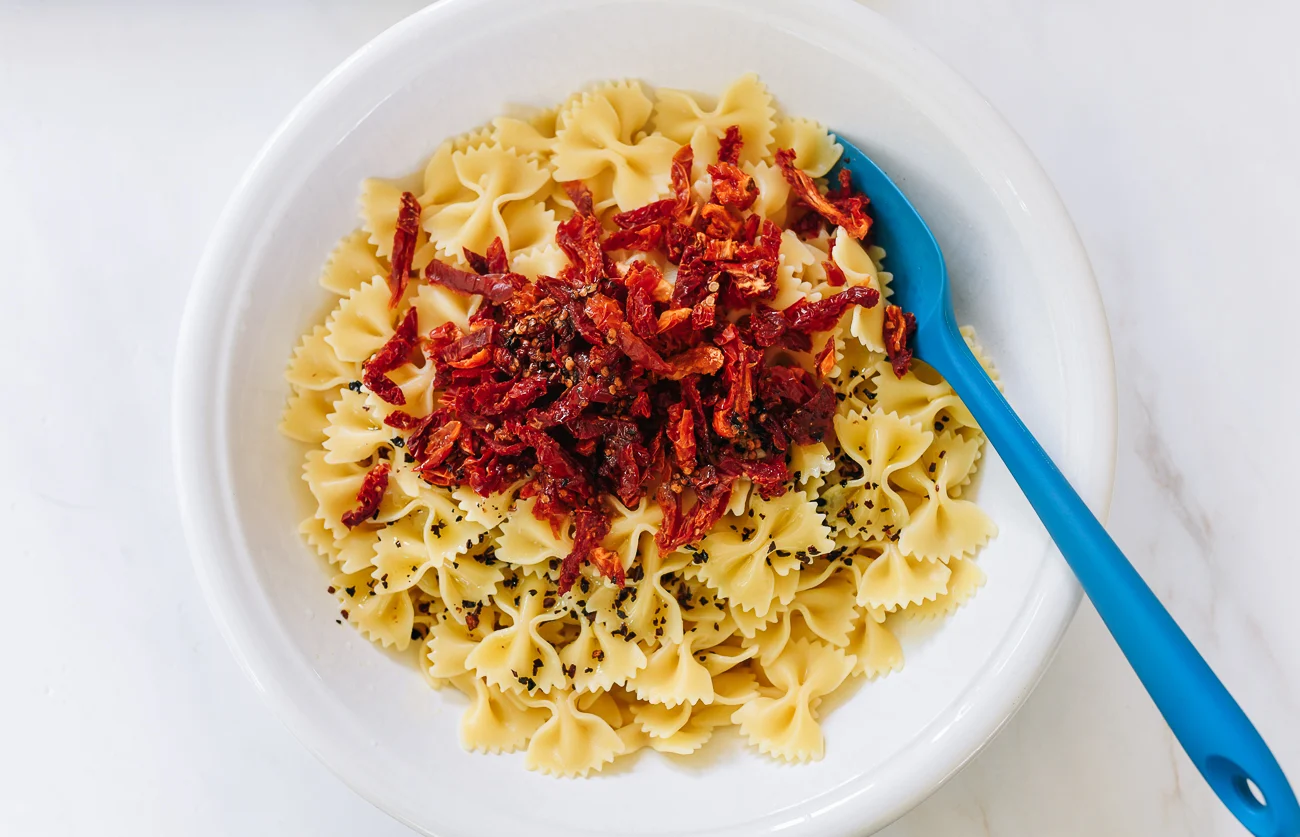 mixing olive oil and sun-dried tomato into pasta salad