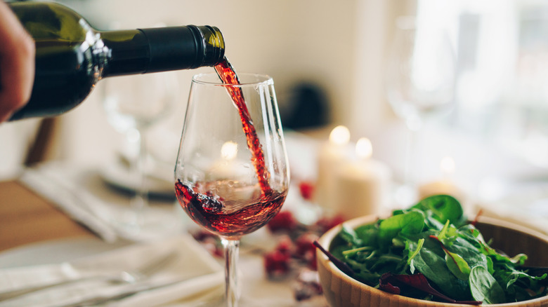 Red wine being poured at the dinner table next to bowl of salad greens
