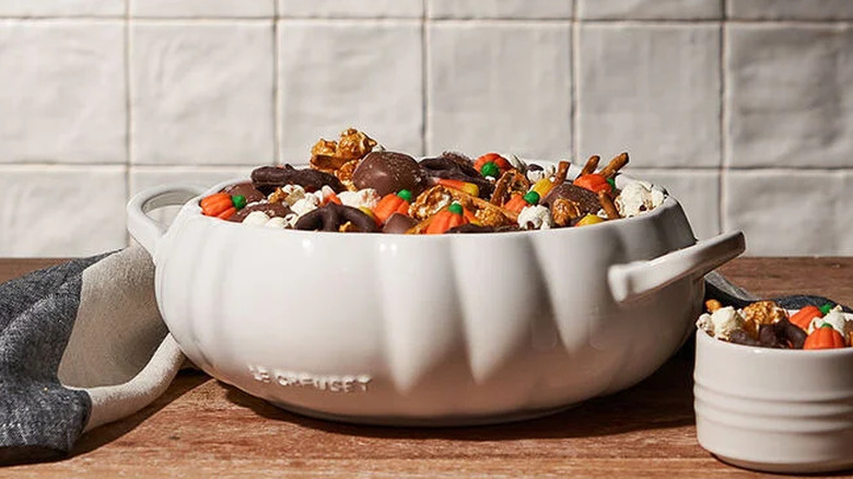 The Pumpkin Serving Bowl in white overflowing with Halloween candy next to an overflowing ramekin of candy.