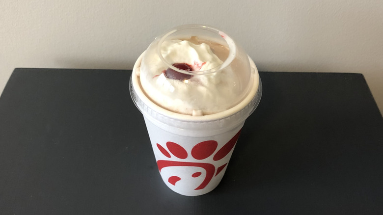 Chocolate milkshake from Chick-fil-A in a to-go cup, resting on a black table