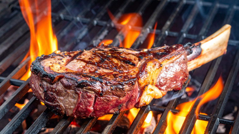 Tomahawk steak with a large bone cooking on a flaming grill