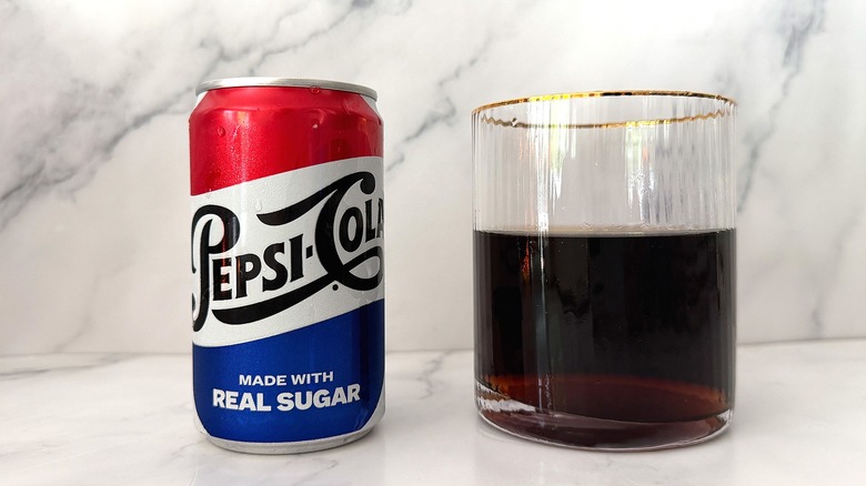 Can of Soda Shop Pepsi next to gold-rimmed glass of Pepsi on marble surface
