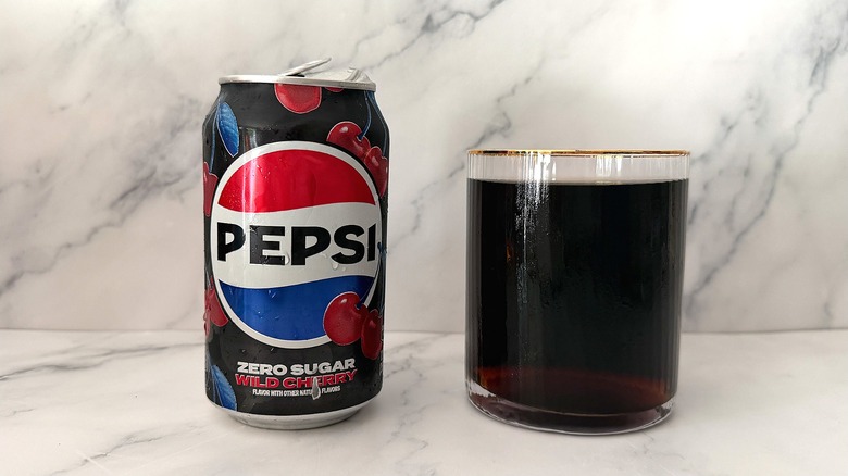 Can of Zero Sugar Wild Cherry Pepsi next to gold-rimmed glass of Pepsi on marble surface