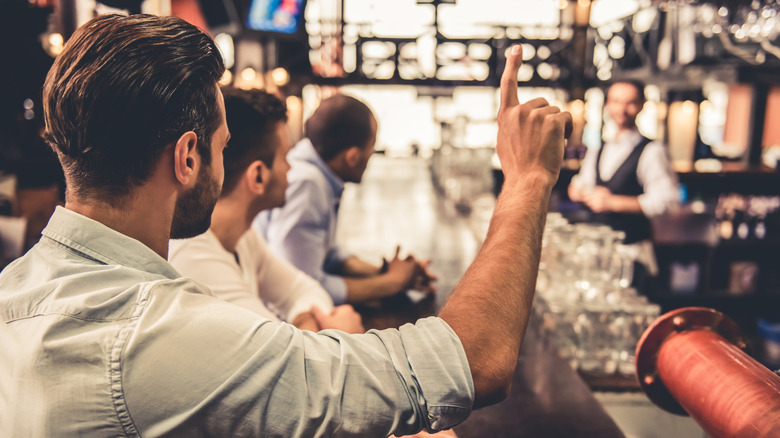 Man trying to get a bartender's attention at a bar