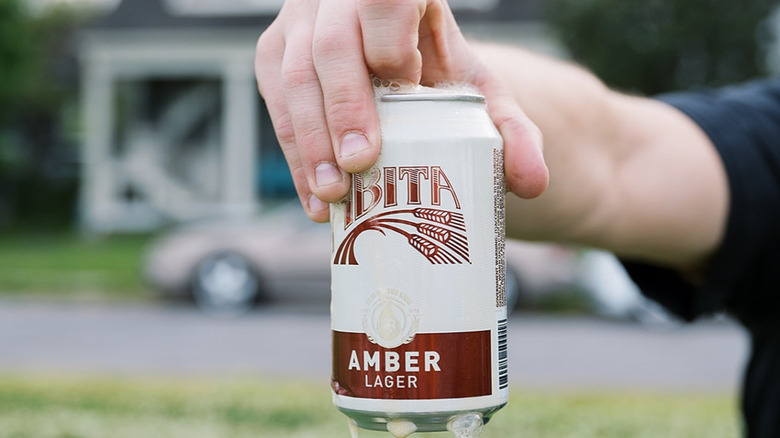 A person holding up a just-opened can of Abita Amber as the beer froths out of the can