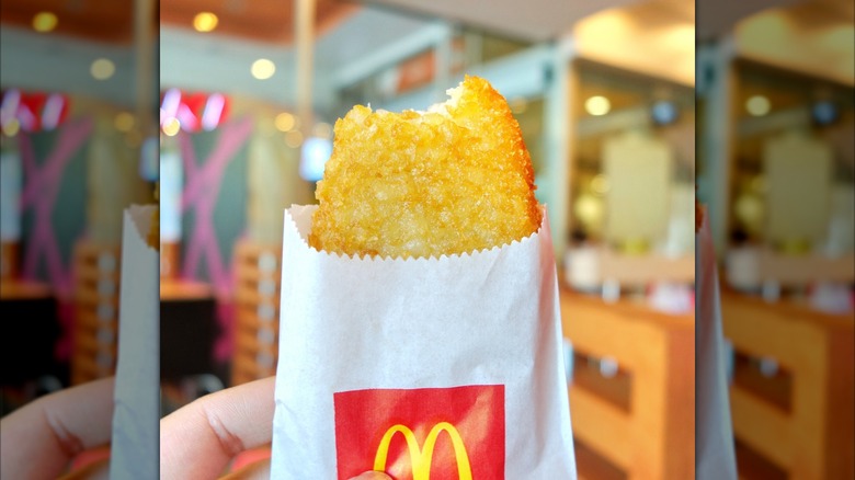 A hand holding a McDonald's hash brown in its paper sleeve