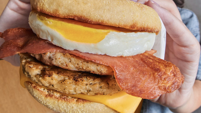 A close up of an Egg McMuffin with bacon and two sausage patties