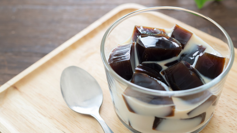 A glass of Japanese coffee jelly next to spoon on wooden board