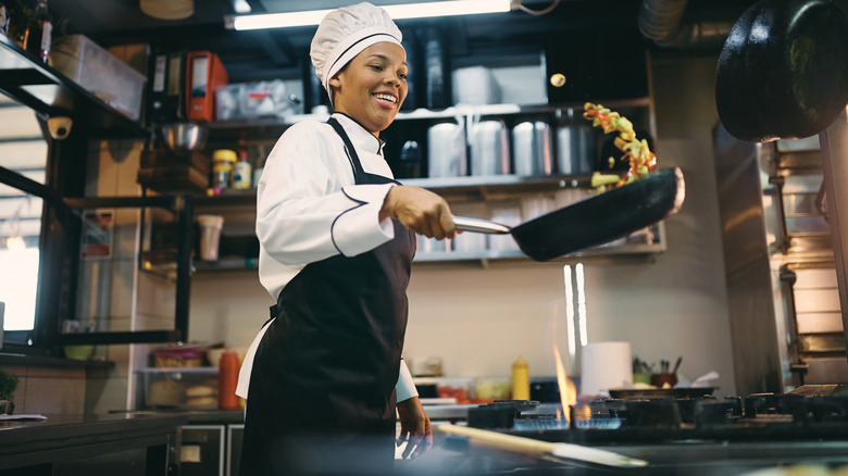 A female chef gleefully prepares vegetables in a pan.