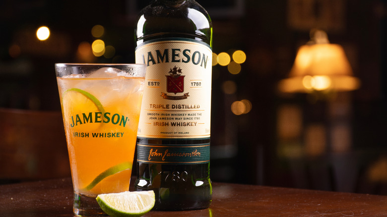 A bottle of Jameson on a table next to a cocktail in a branded glass