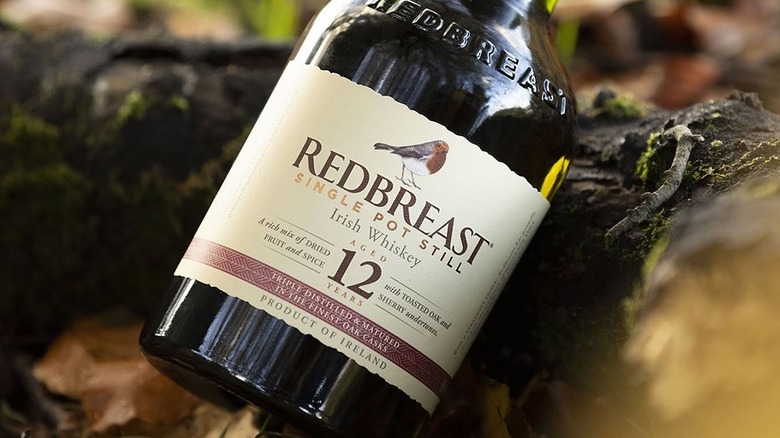 A close-up shot of a bottle of Redbreast 12-year resting against a log outdoors