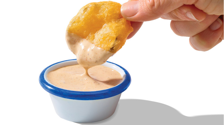 A closeup of a hand dipping a fried pickle in Ranch with Old Bay seasoning.