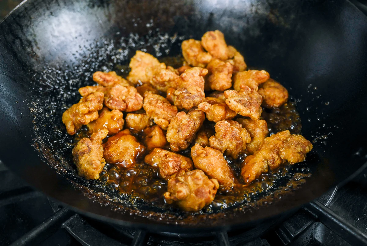 fried chicken pieces added to sauce in wok