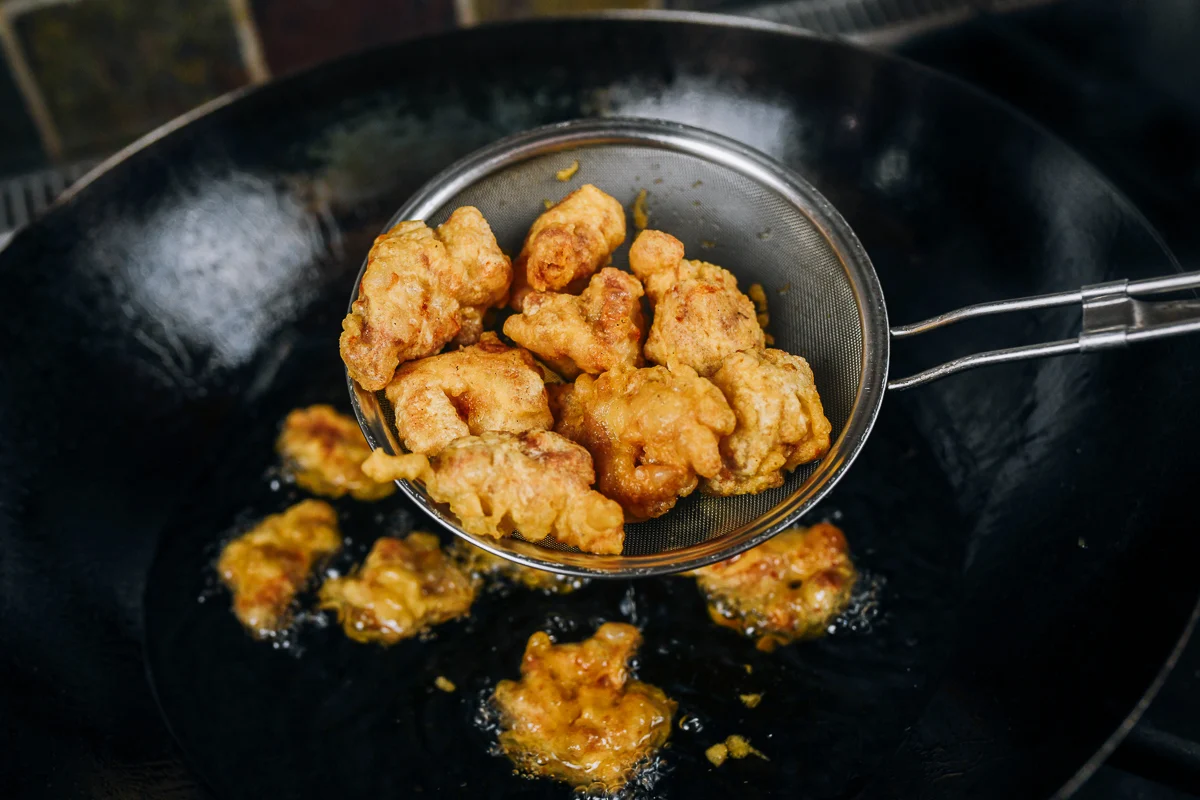 pulling fried chicken pieces out of oil after first fry