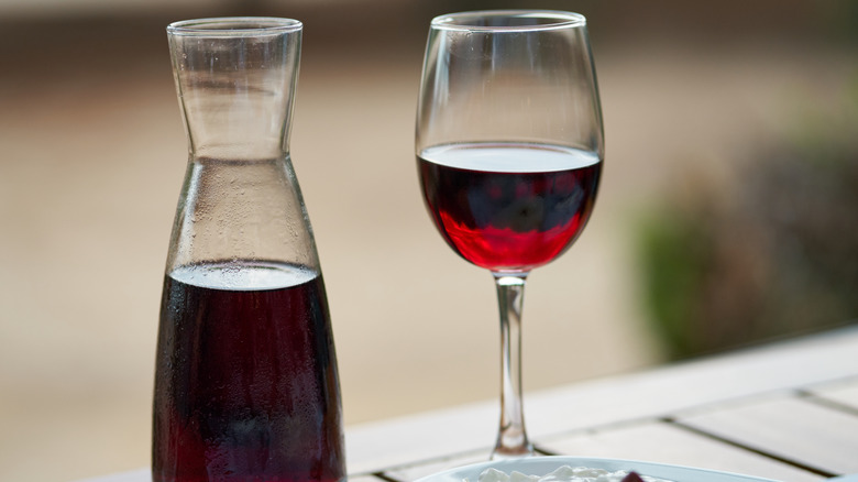 A glass of red wine next to a full carafe on a table