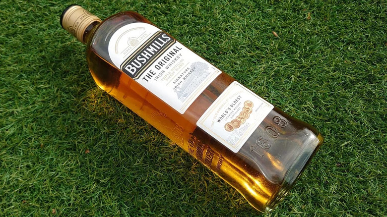 A bottle of Bushmills Original placed on artificial grass, with sunlight shining through it