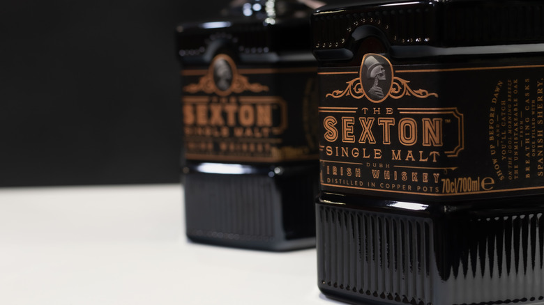 Two bottles of The Sexton Single Malt on a white table in front of a plain black background