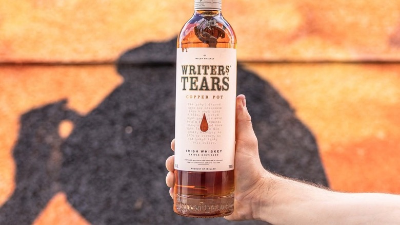A bottle of Writers' Tears Copper Pot held up to the camera, with a shadow shown on a blurry background