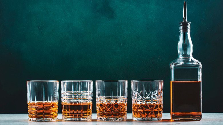 Four filled glasses of whiskey lined up next to an unbranded bottle