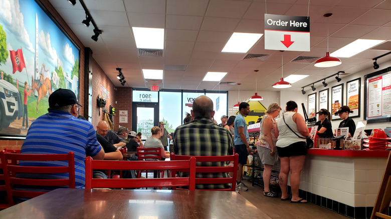View from a table inside a Firehouse Subs, people and line in background