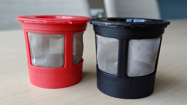 A red and black reusable K-cup on a neutral table with grey chairs in the background