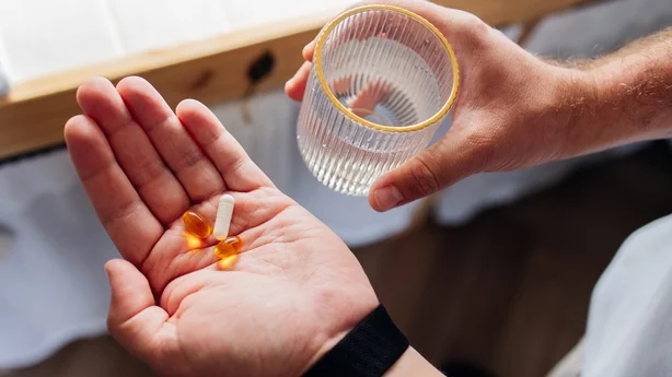Close-up of person preparing to take vitamin supplements with glass of water at home. Daily wellness, healthcare routine and self care concept.