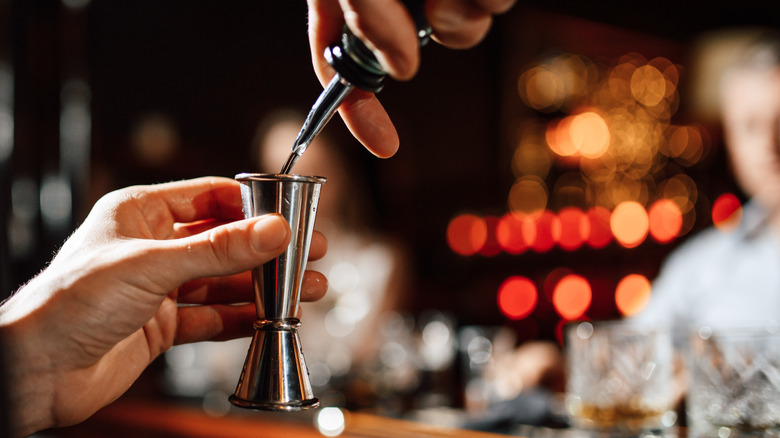 A close shot of a bartender pouring a measure into a jigger with a blurred background
