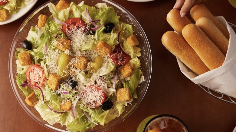 Olive Garden salad sprinkled with grated cheese and served alongside breadsticks
