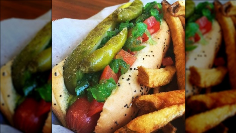 Deep-fried hot dog drizzled with sauces next to tater tots on white plate