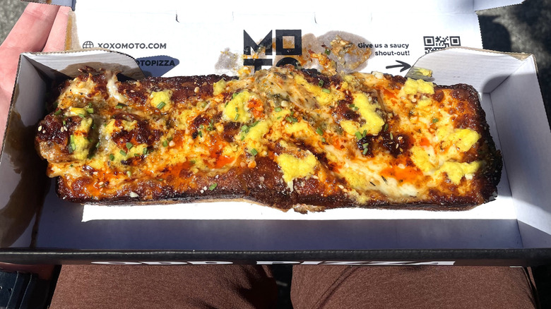 A Detroit-style square-cut pizza with pineapple on top in a cardboard box